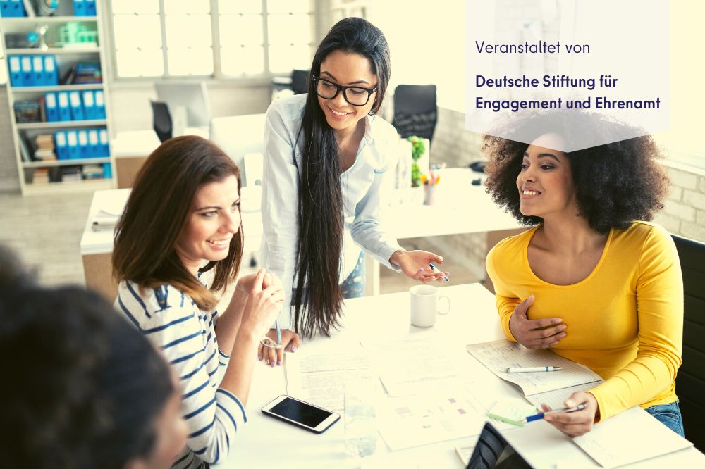 Drei Frauen sitzen an einem Schreibtisch und interagieren miteinander.