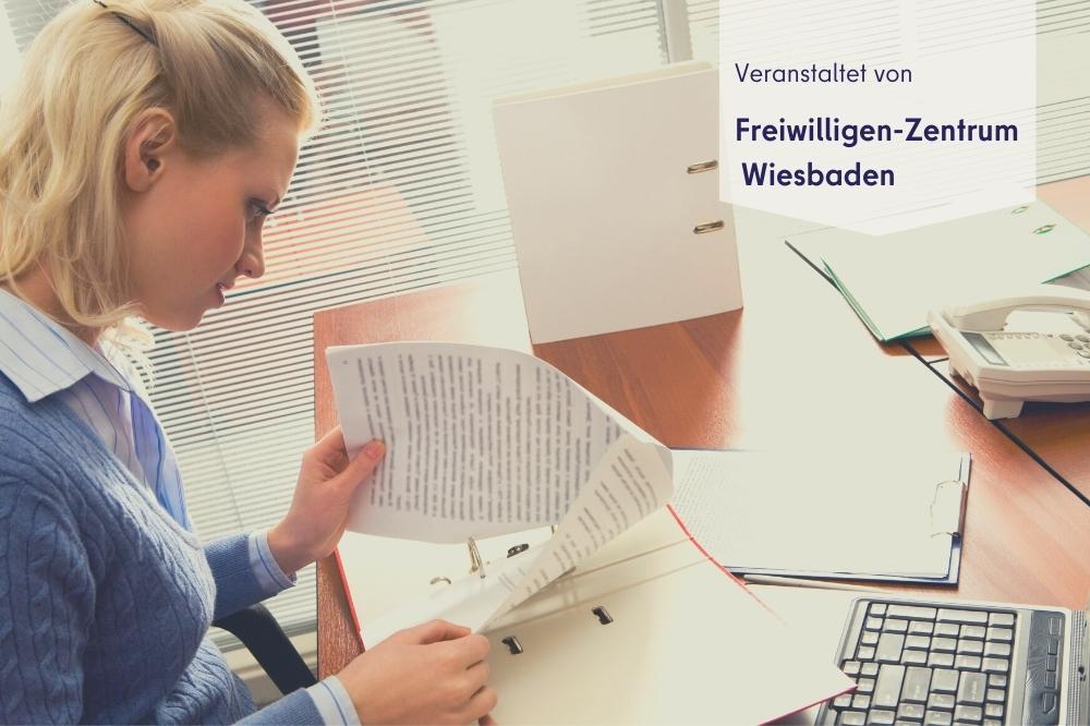 Auf dem Bild sieht man eine Frau über Unterlagen an einem Schreibtisch sitzen. Rechts oben steht "Veranstaltet von: Freiwilligen-Zentrum Wiesbaden" geschrieben.